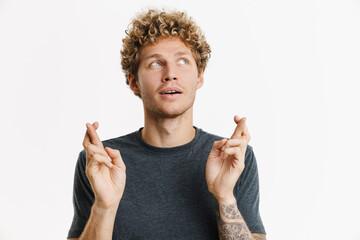Young blonde man holding fingers crossed for good luck