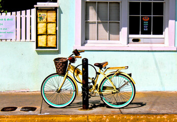 Fototapeta na wymiar Bright yellow bicycle parked on a sidewalk, leans against a post near a colorful building