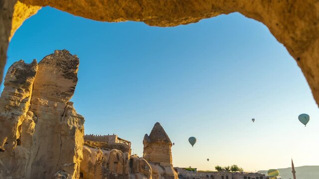 4k stock photography video time lapse of amazing ancient architecture of Cappadocia and many hot air ballons flying in morning sky over buildings and hotels of Goreme town. Turkey