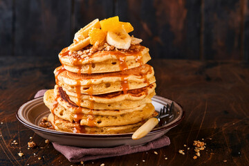 Pancakes. Homemade fluffy pancake with banana, walnut and caramel for breakfast on dark wooden background. Delicious pancakes for traditional American breakfast. Selective focus. Mock up. - obrazy, fototapety, plakaty