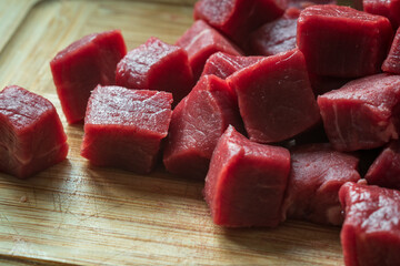 cubes of sliced raw roast beef meat on wooden cutting board closeup
