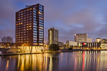 Fototapeta na wymiar Rotterdam, The Netherlands, January 17, 2022: view of Coolhaven harbour with several residential and educational buildings at its banks, during the blue hour on a winter morning
