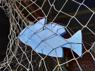 Decorative blue wooden fish hanging on fishing net. Sea life craft. Rustic and vintage decoration. Fishing net with ornamental fish.