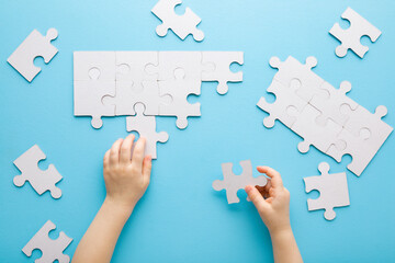 Baby boy hands playing and putting together white puzzle pieces on light blue table background. Pastel color. Closeup. Point of view shot. Children development. Top down view. - obrazy, fototapety, plakaty