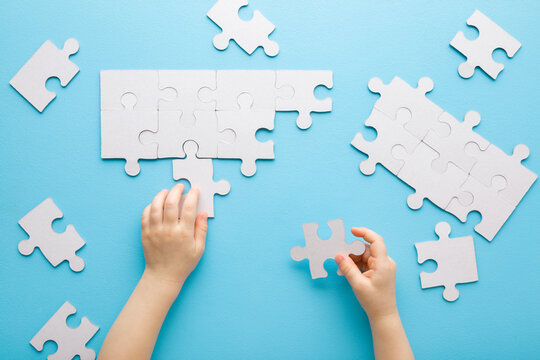 Baby boy hands playing and putting together white puzzle pieces on light blue table background. Pastel color. Closeup. Point of view shot. Children development. Top down view.
