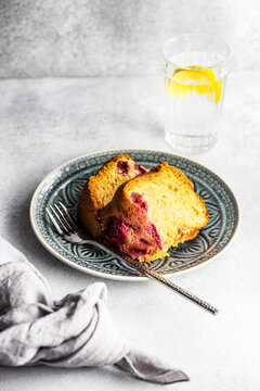 Slice of blueberry and cherry sponge cake on a plate with a glass of lemon water