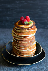 Stack of pancakes for breakfast with raspberries and mint on dark background