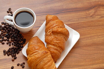 On the table is a cup of espresso and two croissants with a beautiful crispy crust.