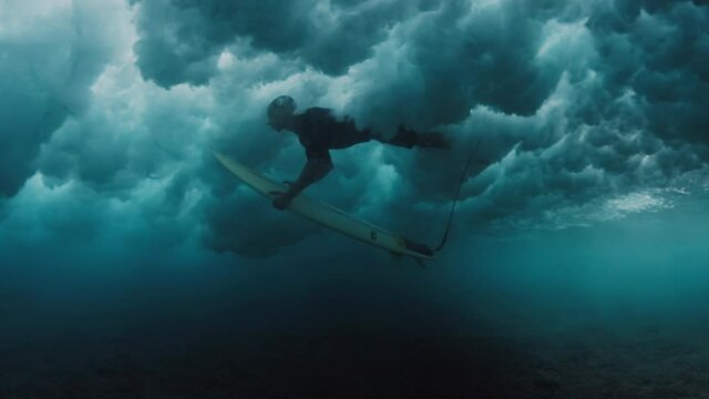 Surfing in Maldives. Man dives with surf board underwater to pass the ocean wave