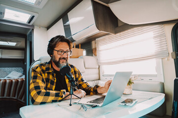 Young adult use microphone and laptop computer to podcast web content inside a camper van. Digital...