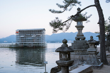 Hiroshima, Japan - November 19, 2021: Great Torii Gate under restoration and stone lanterns in...