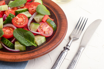 Vegetable salad with tomatoes, sweet peppers, spinach, red onion, cucumber on a white concrete background