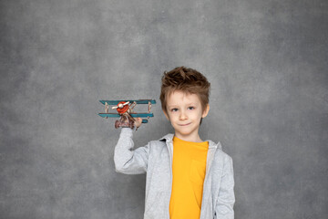 Cute boy playing with wooden airplane toy flying over the gray wall at home. Happiness and freedom