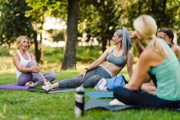 Multiracial women talking and smiling during yoga practice in park