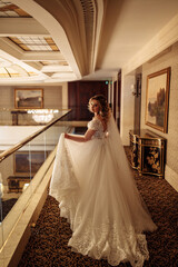 The bride in a white dress in front of the mirrors in the living room. Preparing for the upcoming wedding. Burgundy background.