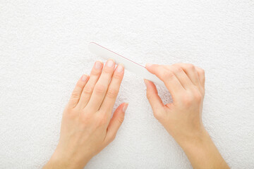 Young adult woman hand using nail file and filing nails on white towel background. Closeup. Point...