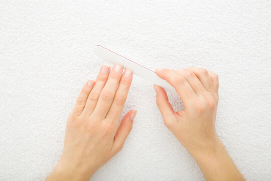 Young adult woman hand using nail file and filing nails on white towel background. Closeup. Point of view shot. Care about fingernails. Top down view.