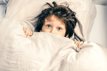 Scared child covering half of face with blanket.