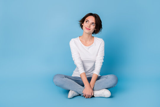Photo of pretty dreamy woman wear white shirt sitting legs crossed looking empty space isolated blue color background
