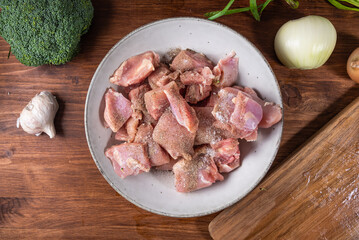Healthy cuisine cooking chicken with vegetables - raw chicken pieces sprinkled with pepper and salt in a bowl, broccoli, onion and garlic