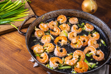 Shrimps fried with green onions in a pan, close-up on a wooden table