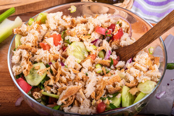 Cooking vegetarian panzanella salad with tomatoes, red onion, breadcrumbs, cucumbers in a glass bowl - close-up