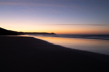 Fototapeta na wymiar Tregantle Beach in Whitsand Bay Cornwall at sunrise with reflections in the sand and sea