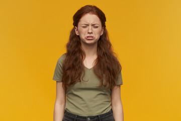 Indoor portrait of young ginger female keeps her eyes closed while crying. isolated over yellow background