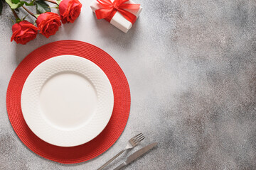 Valentine's day festive dinner with red roses, gift and red rose flowers on gray background. Top view. Copy space.