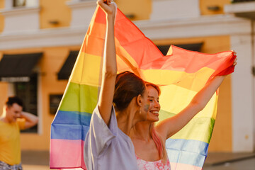 Young lesbian couple walking with rainbow flag during pride parade