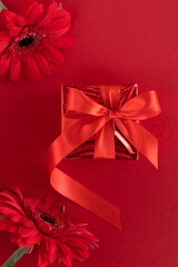 gift box with ribbon, gerbera flower on red background.  valentines day, birthday party, love concept. greeting card. vertical