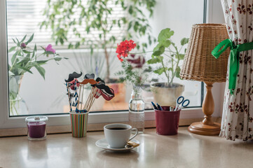 Work area in the home, a window-sill, a lot of plants, a lamp with a shade, curtains in a flower and a cup of coffee with chocolate.
