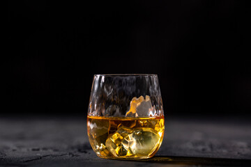 Glass of whiskey with ice placed in front of black background