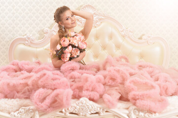 Portrait of beautiful young woman in pink dress sitting on bed