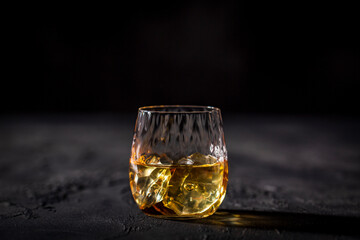 Glass of whiskey with ice placed in front of black background