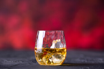 Glass of whiskey with ice placed in front of red background