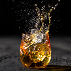 Glass of whiskey splashing with ice thrown into it on black background