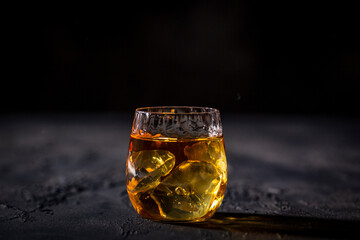 Glass of whiskey with ice placed in front of black background