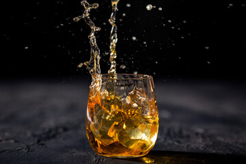 Glass of whiskey splashing with ice thrown into it on black background