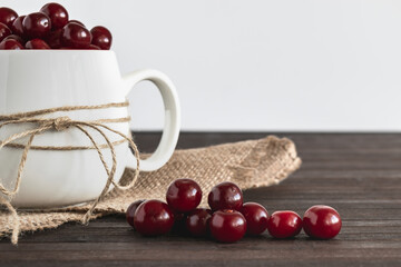 A white porcelain mug with cherries and berries scattered nearby on a wooden table.