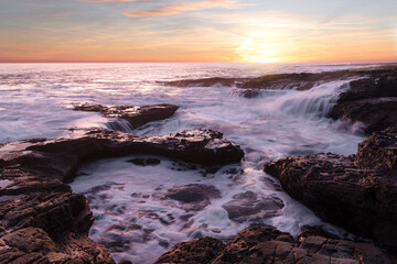 Obraz premium Beautiful sunrise at the coast with amazing vibrant colours and long exposure of the crashing waves 
