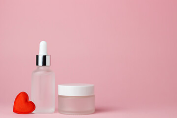 Two white glass cosmetic jars for cream and serum on a pink background with red heart. Cosmetology and beauty. Self care. Model for cosmetics.