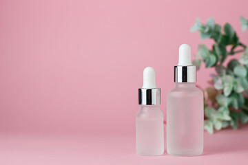 Two white glass cosmetic jars for cream and serum on a pink background with green foliage. Cosmetology and beauty. Self care. Model for cosmetics.