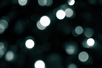 Tidewater Green colors. Defocused bokeh christmas white lights on dark green background. Blurred abstract green glitter texture. Green bokeh glitter wallpaper for Christmas, New year.