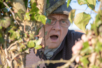 Nosey neighbour peeking through leaves and branches with open mouth and shocked facial expression