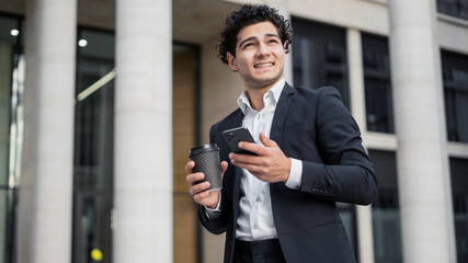 A male manager in an official suit holds a phone in his hands, calls a colleague, drinks coffee