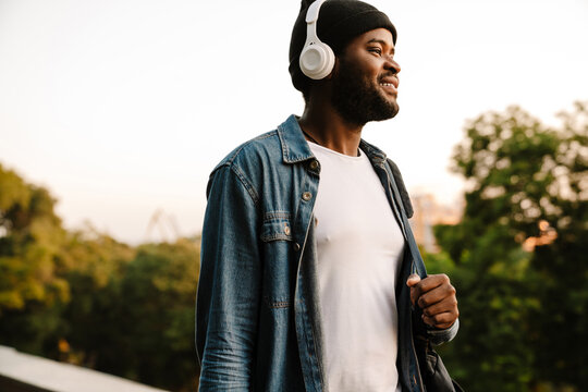 Black man listening music with headphones while walking in park