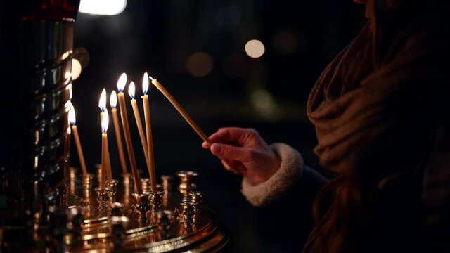 woman in orthodox church, burning candle and praying, parishioner inside temple