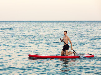 Fototapeta na wymiar Teenager boy learning to paddle on a SUP board in the sea kneeling