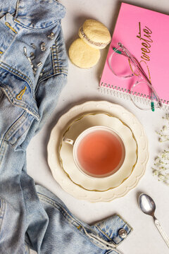 Teacup with macaroons and notepad served on table near scattered denim jacket
